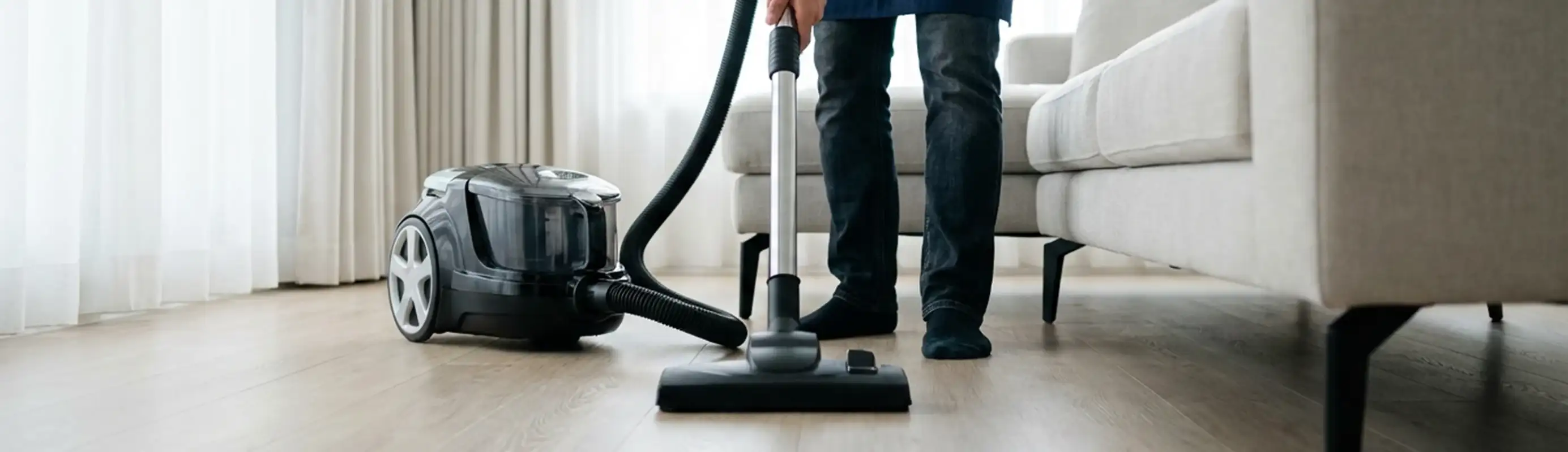 Professional house cleaner vacuuming a living room floor with a canister vacuum cleaner, Detroit, MI.
