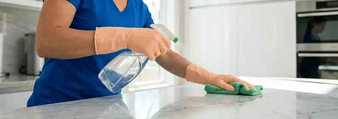 Maid service worker spraying and wiping a kitchen countertop with a microfiber cloth for sanitizing, Detroit, MI.