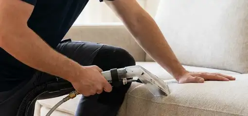 Professional upholstery cleaner deep-cleaning a fabric sofa with a handheld extraction tool, Detroit, MI.