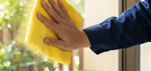 House cleaner wiping a glass window with a yellow microfiber cloth for streak-free cleaning, Detroit, MI.